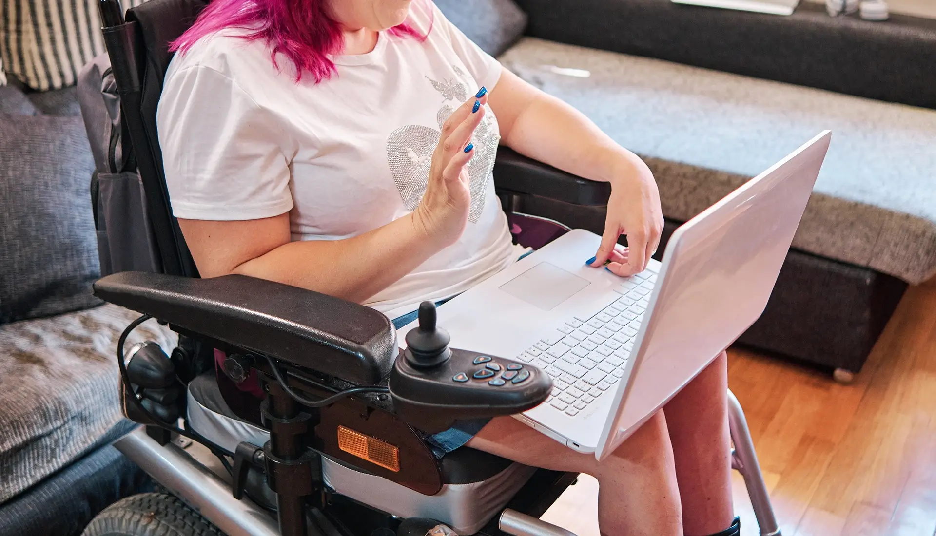 Eine Frau sitzt in einem elektrischen Rollstuhl und nimmt per Laptop an einem Videocall teil.