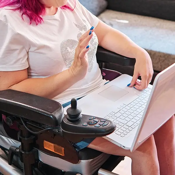 Eine Frau sitzt in einem elektrischen Rollstuhl und nimmt per Laptop an einem Videocall teil.